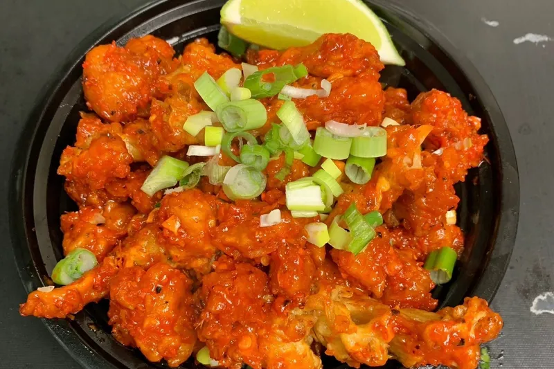 Gobi 65 (crispy fried cauliflower tossed in red chili sauce with scallions and a lime wedge) in a black takeout bowl at Biryani Maxx Indian Cuisine in Cary