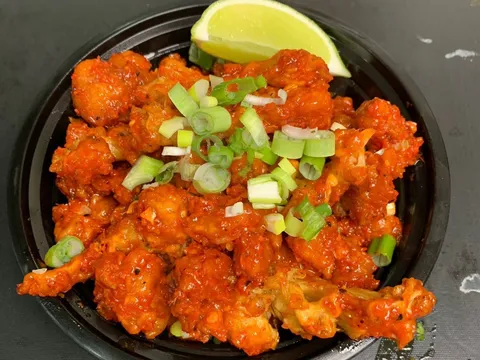Gobi 65 (crispy fried cauliflower tossed in red chili sauce with scallions and a lime wedge) in a black takeout bowl at Biryani Maxx Indian Cuisine in Cary