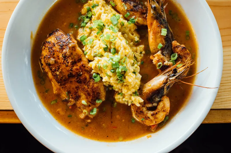 A bowl of Cajun-style blackened chicken and head-on Gulf shrimp over rice in a rich broth, topped with scallions, at Toups' Meatery
