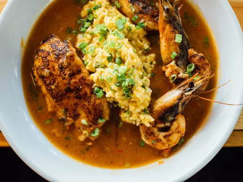 A bowl of Cajun-style blackened chicken and head-on Gulf shrimp over rice in a rich broth, topped with scallions, at Toups' Meatery