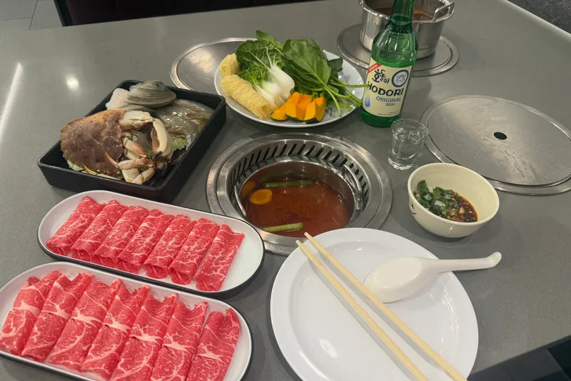 Hot pot spread at Hotpot One in Quincy with platters of sliced marbled beef, seafood and vegetables around a broth-filled pot on a grill table