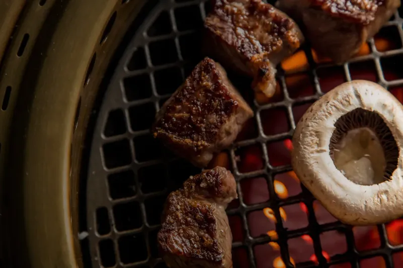 Cubes of beef and a sliced mushroom searing on the tabletop charcoal grill at COTE Korean Steakhouse in New York