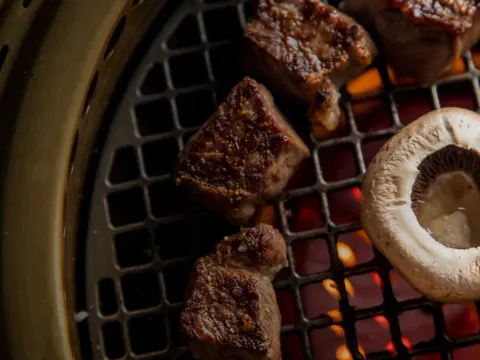 Cubes of beef and a sliced mushroom searing on the tabletop charcoal grill at COTE Korean Steakhouse in New York