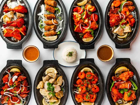 Eight cast-iron sizzler platters of tandoori chicken, seekh kebab, chicken tikka, boti kabab, and tandoori shrimp arranged around a plate of basmati rice at House of India.