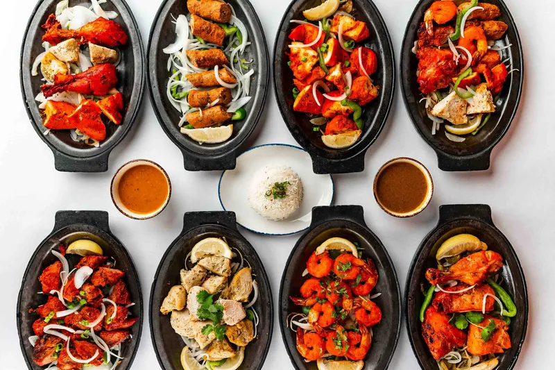 Eight cast-iron sizzler platters of tandoori chicken, seekh kebab, chicken tikka, boti kabab, and tandoori shrimp arranged around a plate of basmati rice at House of India.