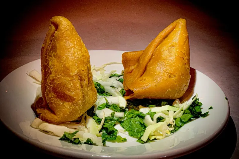 Two golden fried vegetable samosas on a white plate with shredded cabbage and cilantro at Star of India in Little Rock