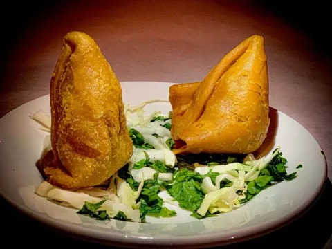 Two golden fried vegetable samosas on a white plate with shredded cabbage and cilantro at Star of India in Little Rock