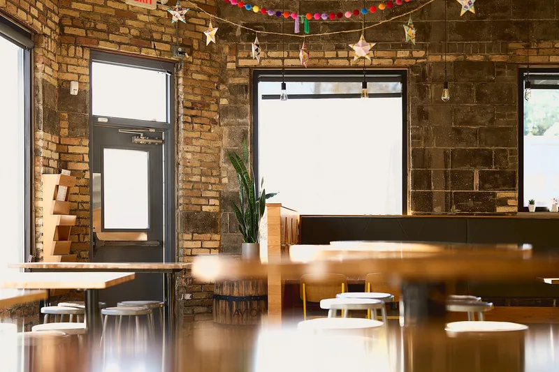 Interior of Donkey Taqueria in Grand Rapids: exposed-brick walls strung with papel picado stars, communal wood tables and stools, and an Avion tequila barrel