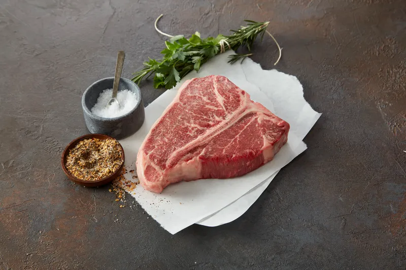A raw T-bone steak with salt, pepper, and herbs at Main Street Meats