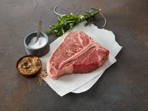 A raw T-bone steak with salt, pepper, and herbs at Main Street Meats