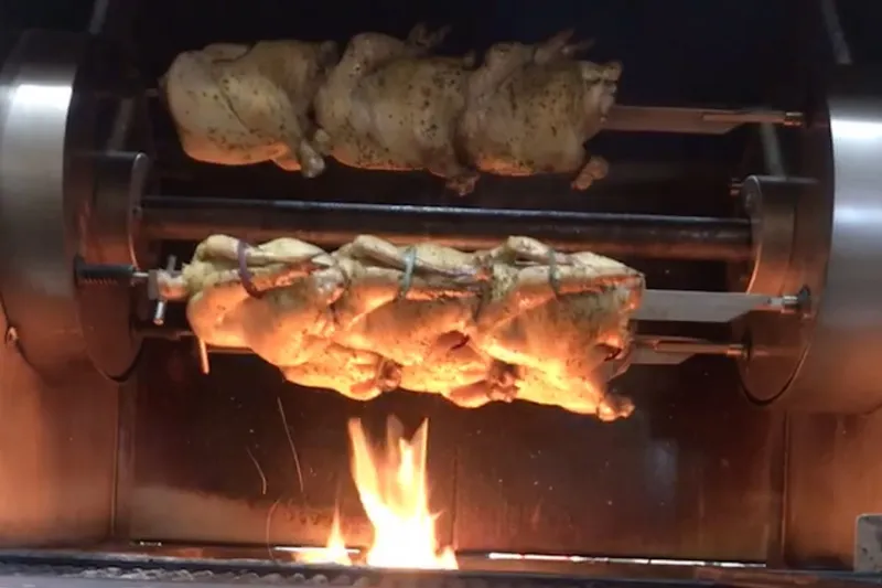 Whole chickens turning on a rotisserie over an open flame at Frontier by Alamo