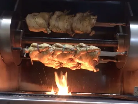 Whole chickens turning on a rotisserie over an open flame at Frontier by Alamo