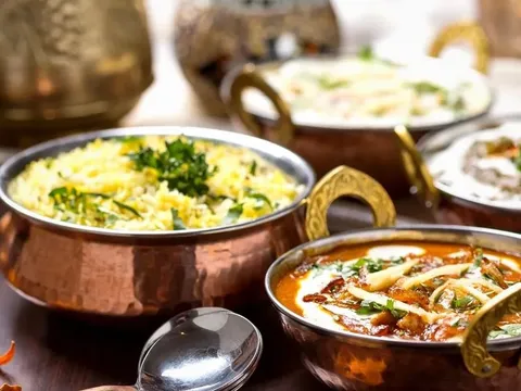 Assorted Royal India dishes served in copper karahi bowls — herbed basmati rice, a creamy tomato curry and other Indian preparations