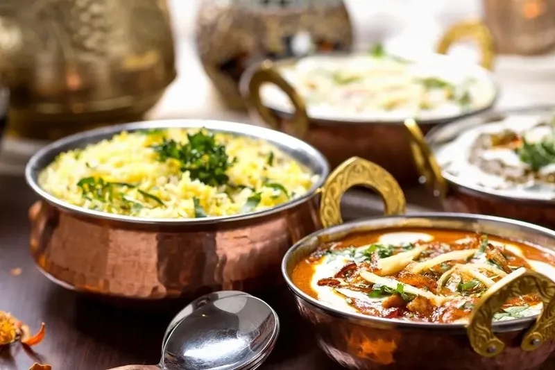 Assorted Royal India dishes served in copper karahi bowls — herbed basmati rice, a creamy tomato curry and other Indian preparations
