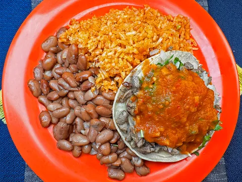 A carne asada taco topped with salsa alongside Mexican rice and pinto beans on an orange plate at Taquería Vallarta