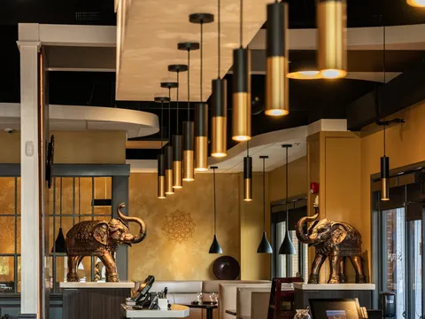 Dining room at Saffron Indian Cuisine in Greenville, with brass elephant statues, black-and-gold pendant lights, a long bar, and the restaurant name lettered on the glass door