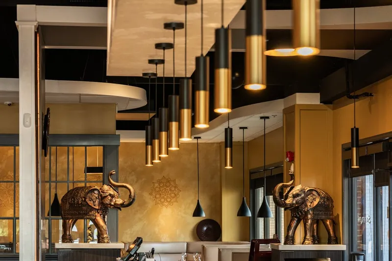 Dining room at Saffron Indian Cuisine in Greenville, with brass elephant statues, black-and-gold pendant lights, a long bar, and the restaurant name lettered on the glass door