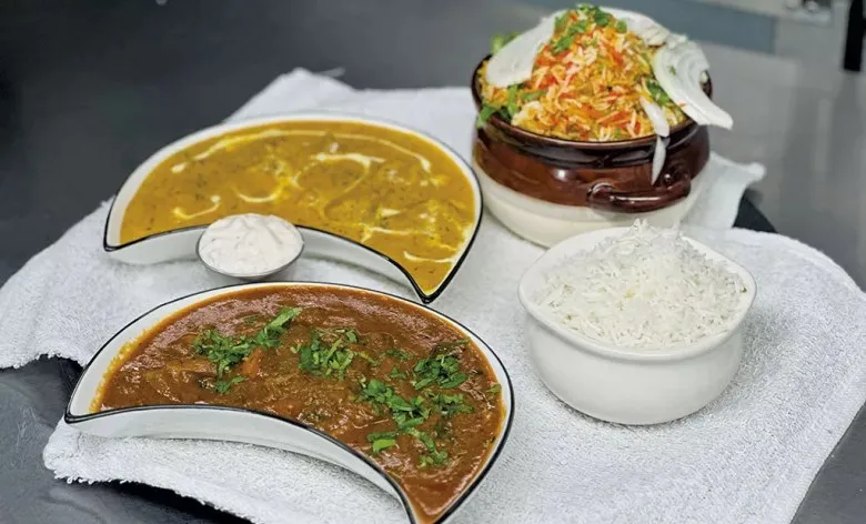 Indian spread at Tikka House in Winooski — a dark curry and a lighter curry in crescent bowls, raita, a pot of chicken biryani and a bowl of basmati rice
