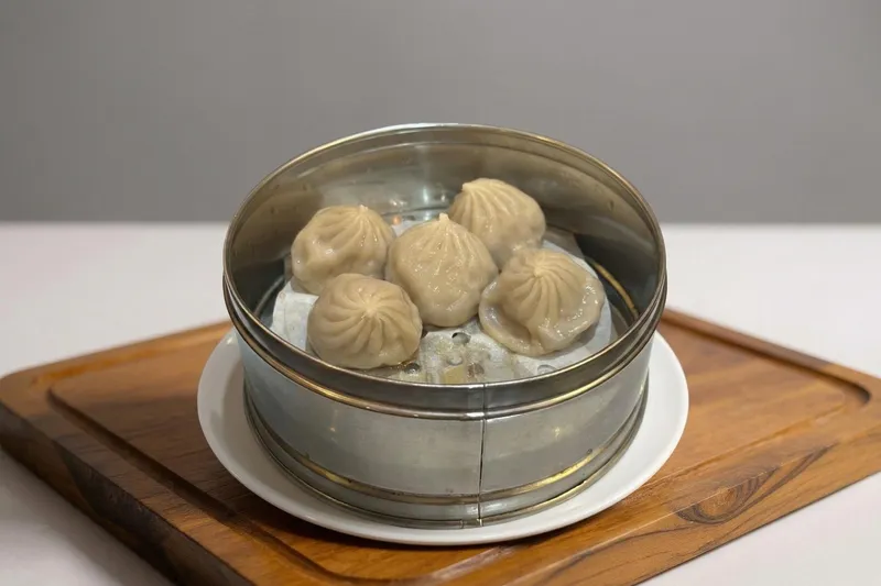 Steamer basket of xiao long bao soup dumplings on a wooden board at Reren Lamen & Bar