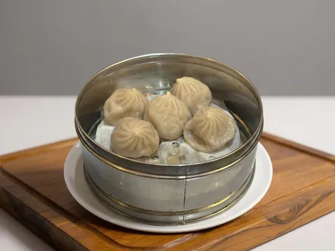 Steamer basket of xiao long bao soup dumplings on a wooden board at Reren Lamen & Bar