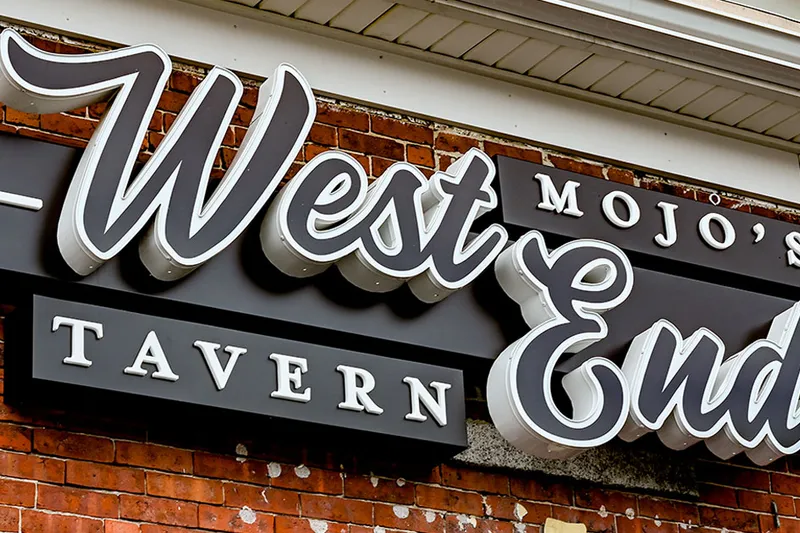 Carved sign reading Mojo's West End Tavern mounted on a brick wall