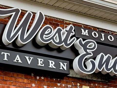 Carved sign reading Mojo's West End Tavern mounted on a brick wall