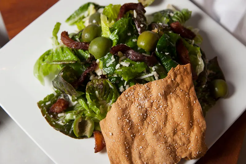 A green salad with olives, bacon, parmesan, and a flatbread cracker at Local 11ten