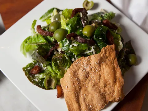 A green salad with olives, bacon, parmesan, and a flatbread cracker at Local 11ten