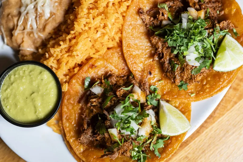 Tacos with a bowl of green salsa at El Beso