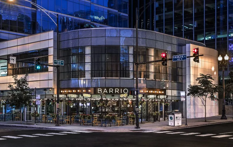 Nighttime exterior of Barrio restaurant at the corner of Clark and Kinzie in River North, Chicago, with its lit BARRIO sign and sidewalk patio