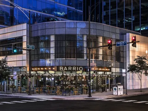 Nighttime exterior of Barrio restaurant at the corner of Clark and Kinzie in River North, Chicago, with its lit BARRIO sign and sidewalk patio