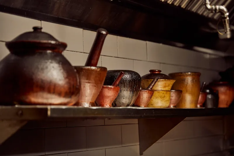 Collection of well-worn clay mortars and cooking pots on a tiled kitchen shelf at Pusadee's Garden Thai restaurant in Pittsburgh
