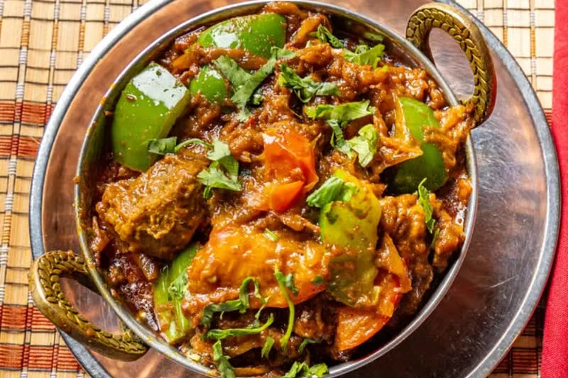 A karahi of India's Restaurant lamb bhoona with green and red bell peppers and cilantro in a copper-handled bowl