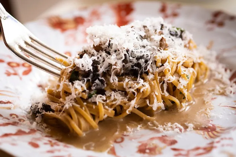 Plate of hand-cut pasta topped with shaved cheese in a light sauce on a patterned plate at Vetri Cucina in Philadelphia