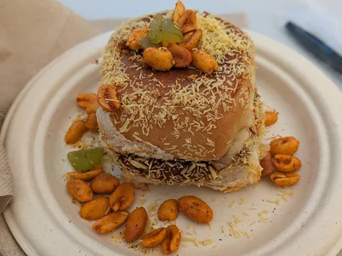 A pav (soft bun) street-food sandwich loaded with fine sev and spiced peanuts on a plate at Pav Bhaji and More, Sunnyvale