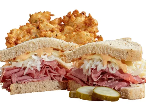 A reuben sandwich piled with corned beef and sauerkraut alongside potato pancakes at Izzy's