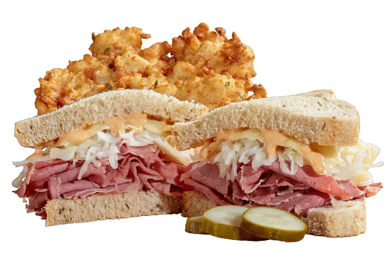 A reuben sandwich piled with corned beef and sauerkraut alongside potato pancakes at Izzy's