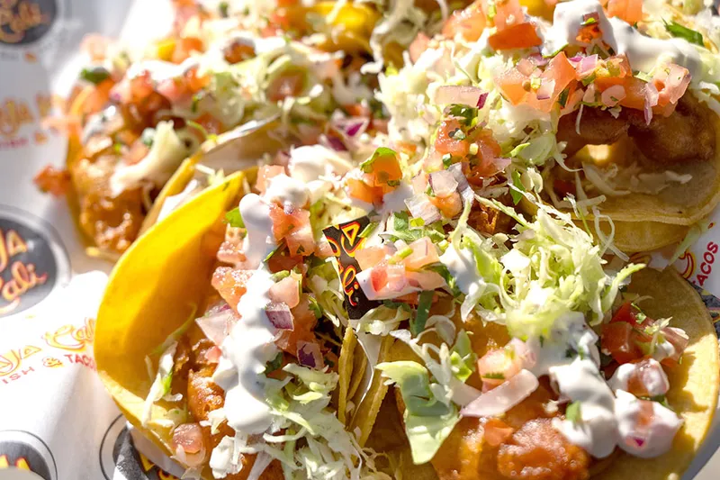 Tray of Baja-style battered fish tacos topped with cabbage, pico de gallo and crema on Baja Cali Fish & Tacos branded paper