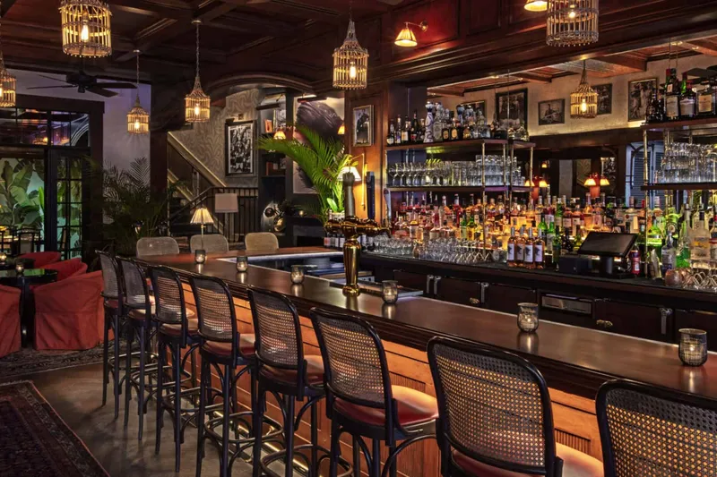 The warmly lit wood bar and lounge at Le Colonial Chicago with birdcage lanterns, cane bar stools and tropical decor