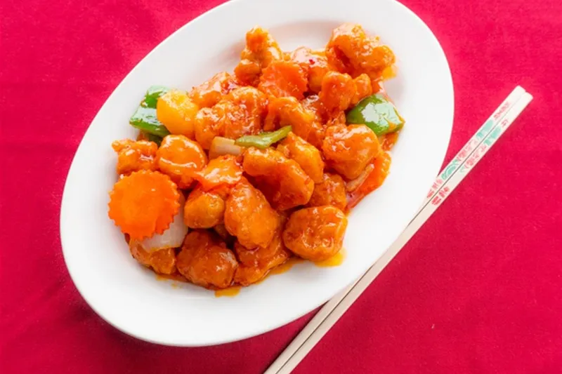 General Tso's chicken — battered chicken pieces in glossy orange chili sauce with green bell pepper and a carved carrot garnish on a white oval plate with chopsticks, at Kung Fu Thai & Chinese Restaurant in Las Vegas