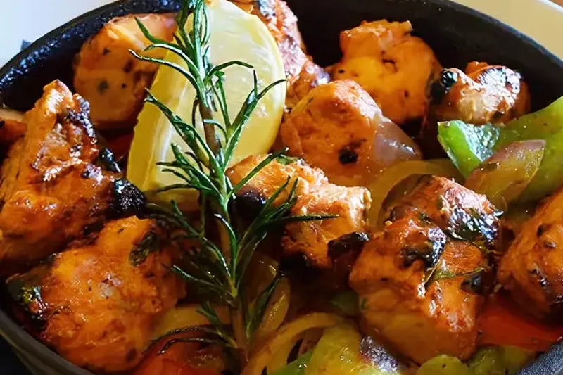 Sizzling chicken tikka with peppers and onions served in a cast-iron skillet at Marigold Maison in Phoenix