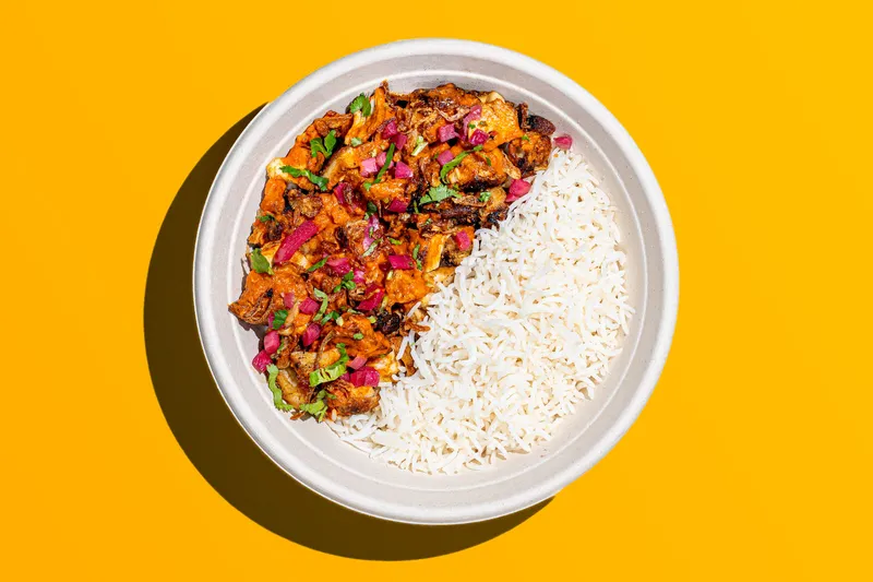 Chicken tikka masala with basmati rice in a round bowl on a bright yellow background