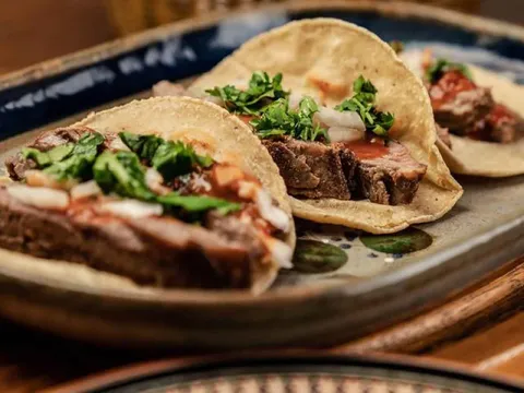 Two bistec tacos on soft corn tortillas topped with cilantro, onion and salsa, served on a blue-rimmed ceramic plate at Mezcal Mexican Cantina