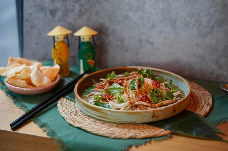 Vietnamese noodle salad in a ceramic bowl with herbs and chili, alongside crab chips and decorative figurines at Turtle Tower