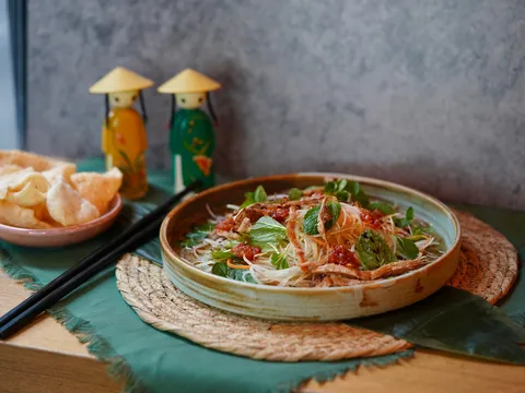 Vietnamese noodle salad in a ceramic bowl with herbs and chili, alongside crab chips and decorative figurines at Turtle Tower