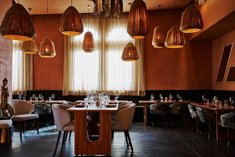 Dining room at Ikara, with terracotta walls, woven pendant lights and set tables