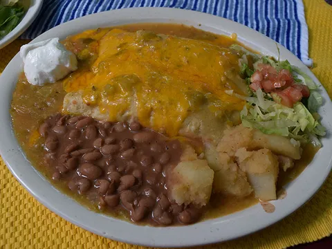 Plate of green chile chicken enchiladas smothered in green chile and melted cheese with sour cream, pinto beans and papas at El Patio de Albuquerque
