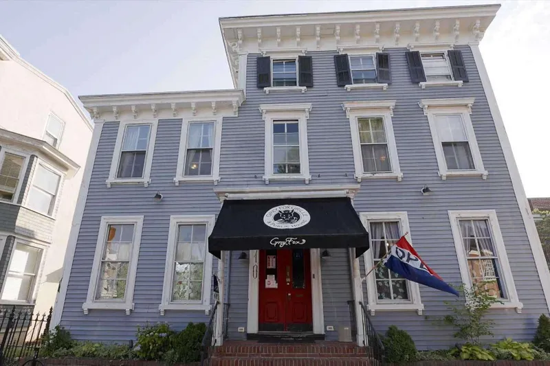 Grey clapboard building with a black awning over the entrance to Grey Fox Grille in downtown Dover
