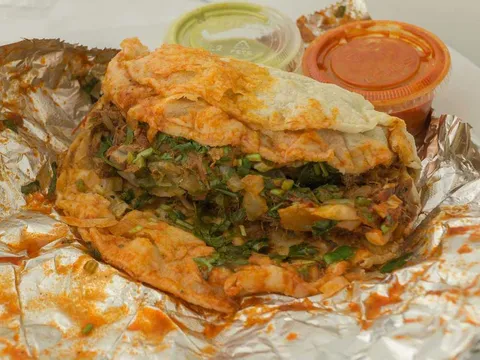Folded quesabirria-style taco with two cups of red and green salsa on foil at El Rey del Taco