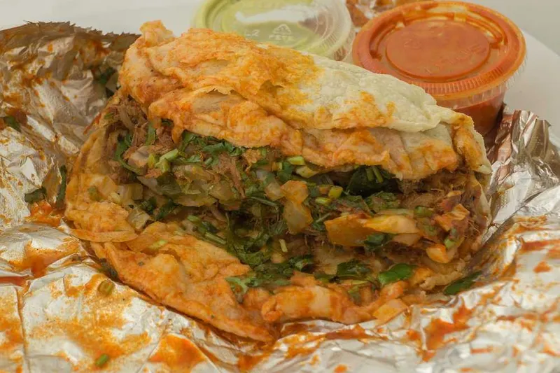 Folded quesabirria-style taco with two cups of red and green salsa on foil at El Rey del Taco